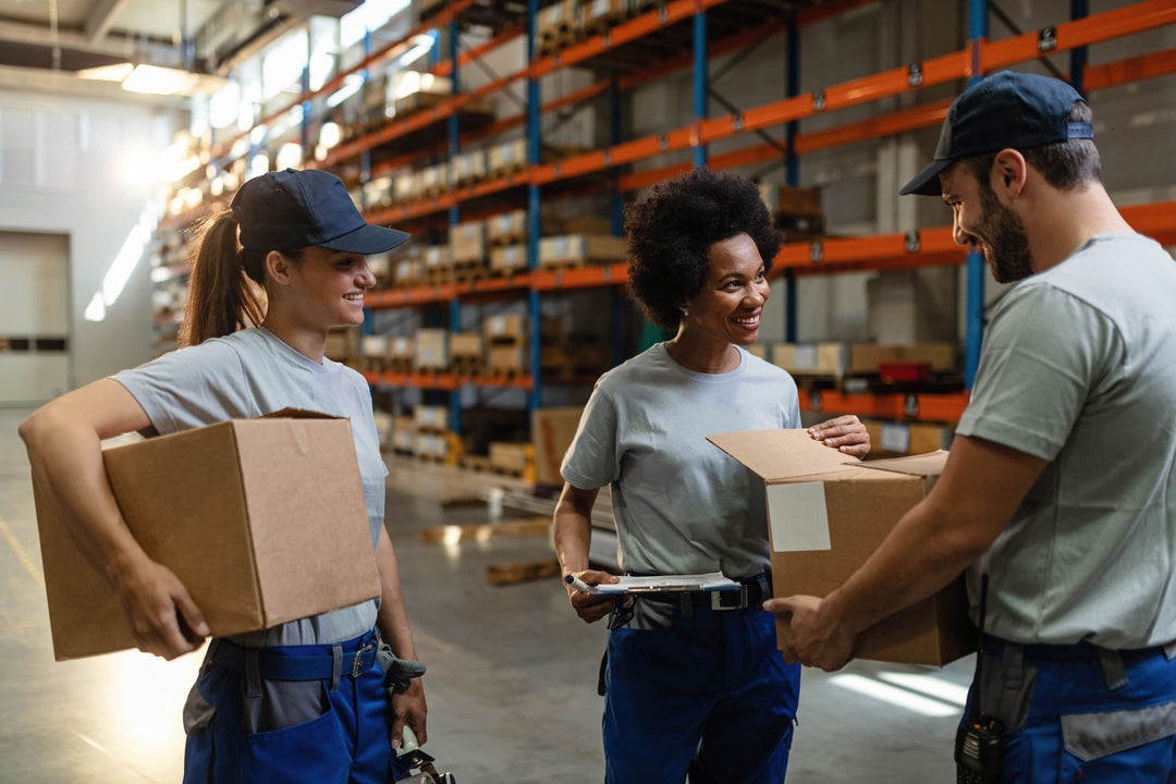Team of warehouse workers smiling and examining packages together in a distribution center.